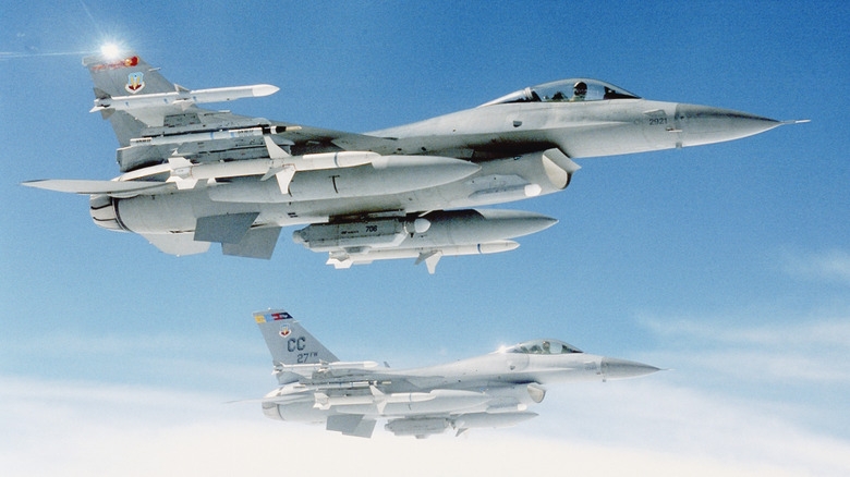 Two F-16s brimming with armament flying in formation in the sky