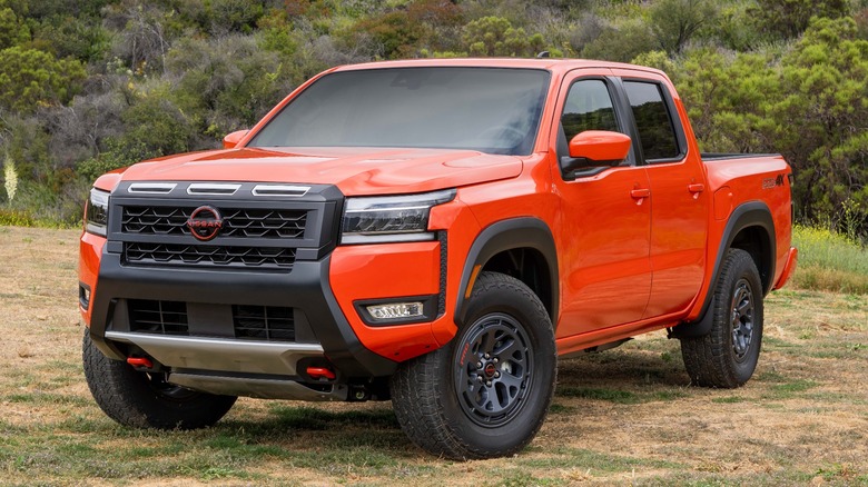 An orange Nissan Frontier on dirt with scrub in the background