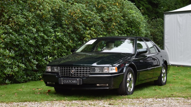 A black 1990s Cadillac STS parked in the grass