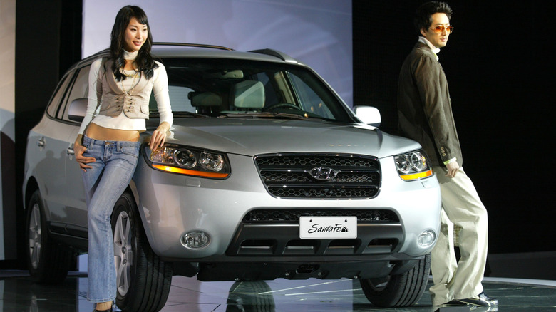 Two models leaning on a gray Hyundai Santa Fe