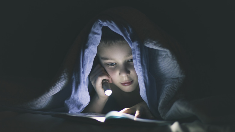 Boy reading under a blanket with a flashlight