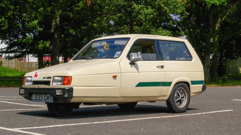 Vintage Reliant Robin faded yellow three wheeled car parke in lot.