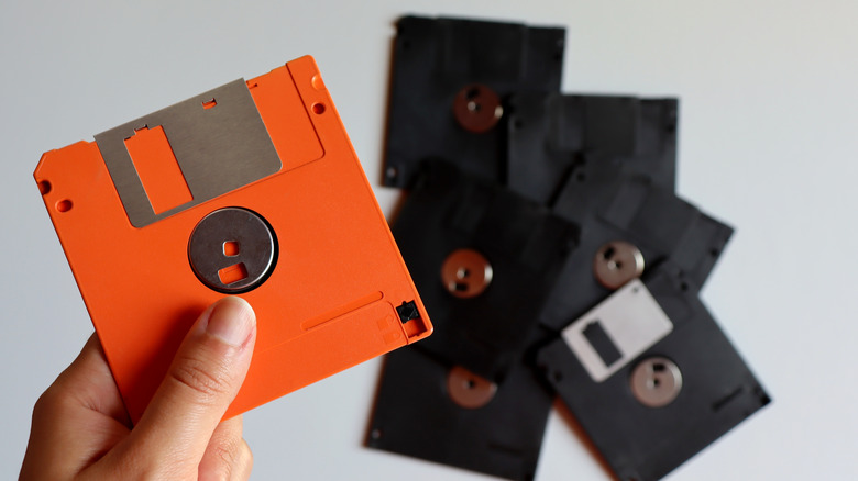 Orange floppy disk in hand, black floppy disks in background