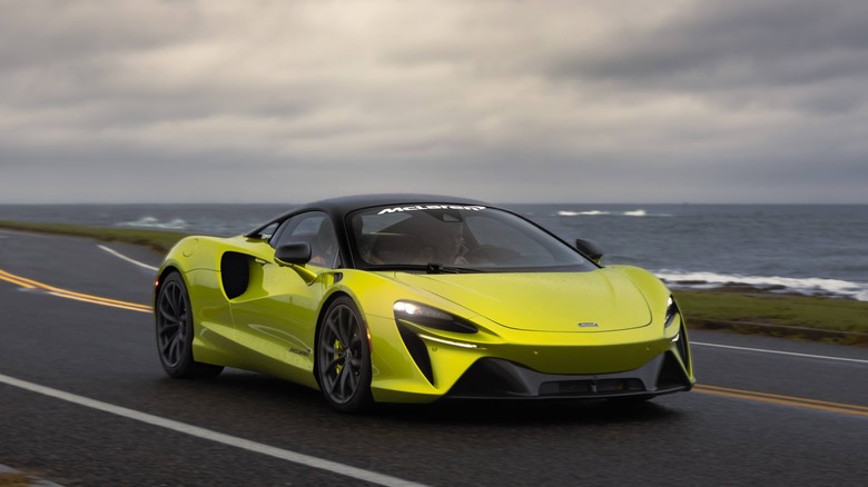 The McLaren Artura in bright green driving along a coast road, front 3/4 view