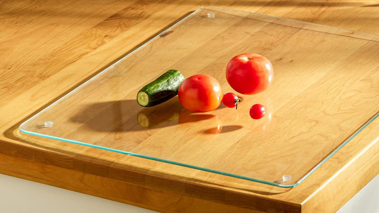 A cucumber and tomatoes on a glass cutting board