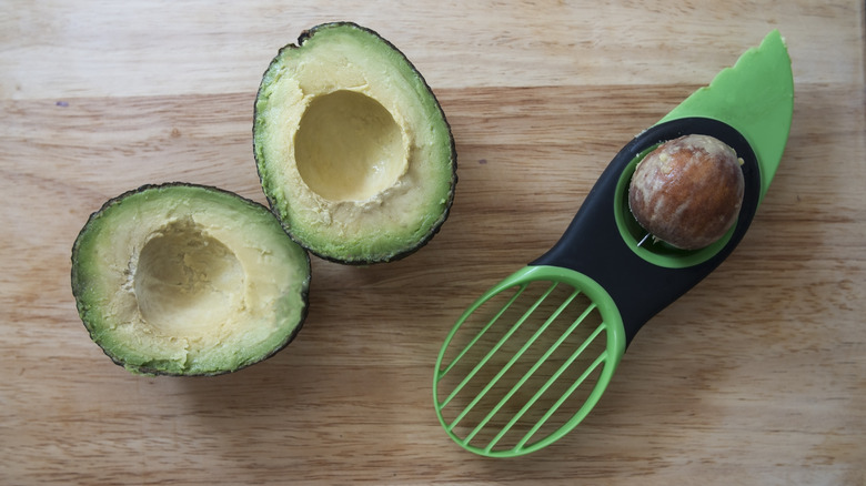 An avocado slicer next to a halved avocado