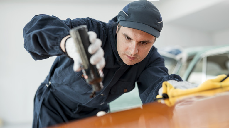 Mechanic applying wax to polish hood of orange car