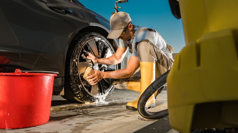 Mechanic washing car rims in sunlight