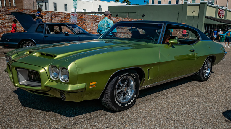 A green 1972 Pontiac GTO cruising up a city street