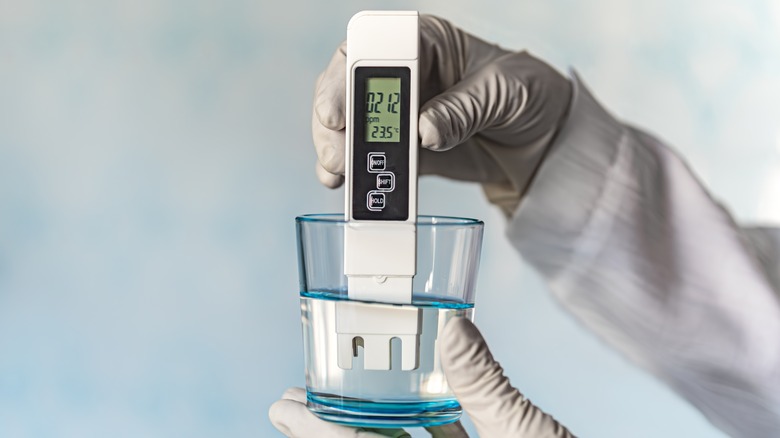 pH meter held by gloved hands, testing drinking water