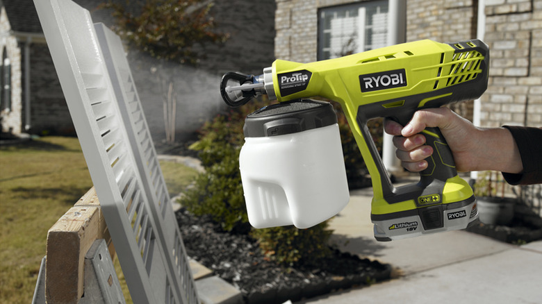 A person painting house trim with a Ryobi paint sprayer