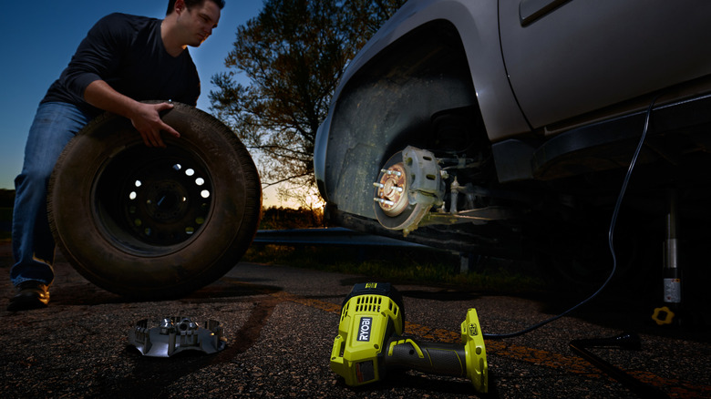 Man changing a car tire using a spotlight as a light source