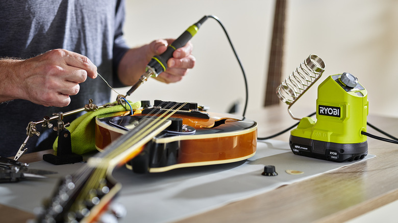 Man fixes guitar with soldering iron