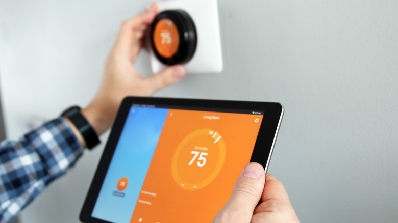 A person adjusts a Nest Thermostat with a tablet