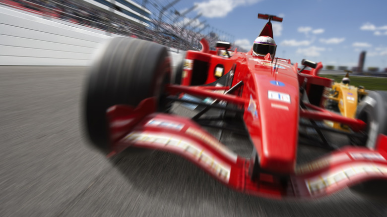 Red formula one race car on track with grandstands behind it.