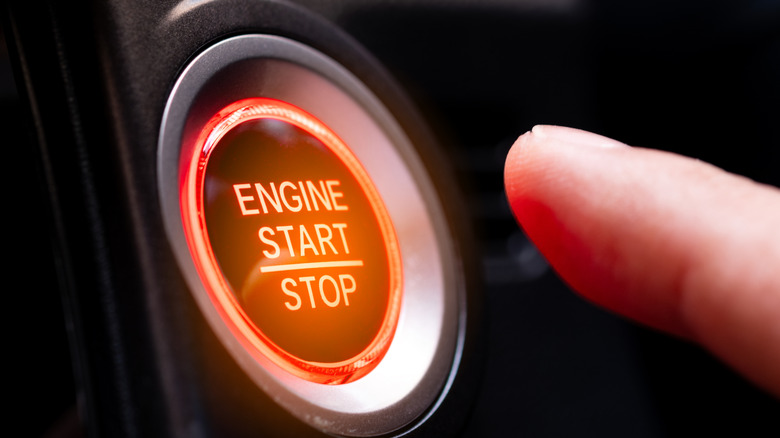 Orange car push start button ignition with finger approaching.