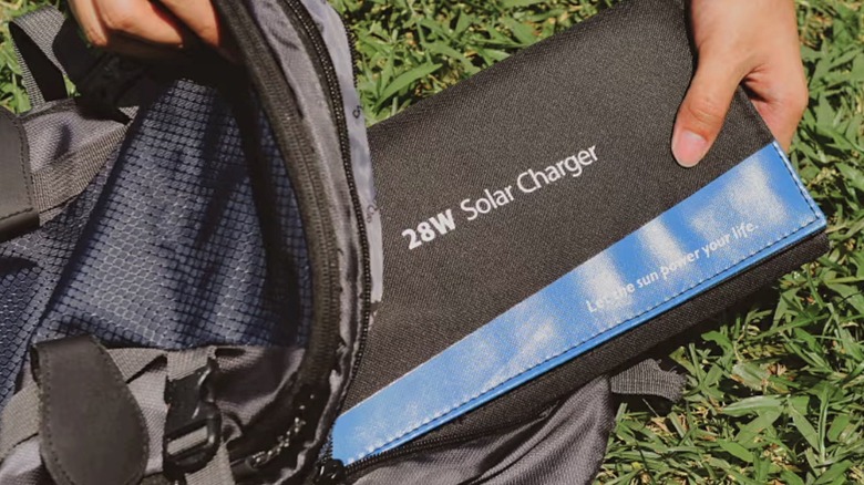 A hiker slipping a folded-down BigBlue SolarPowa 28 solar panel into a backpack.