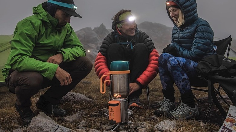 A group of campers sitting around the BioLite CampStove 2+ while it cooks.