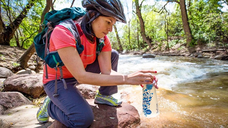 A cyclist fills her Katadyn BeFree Water Filter from a river.