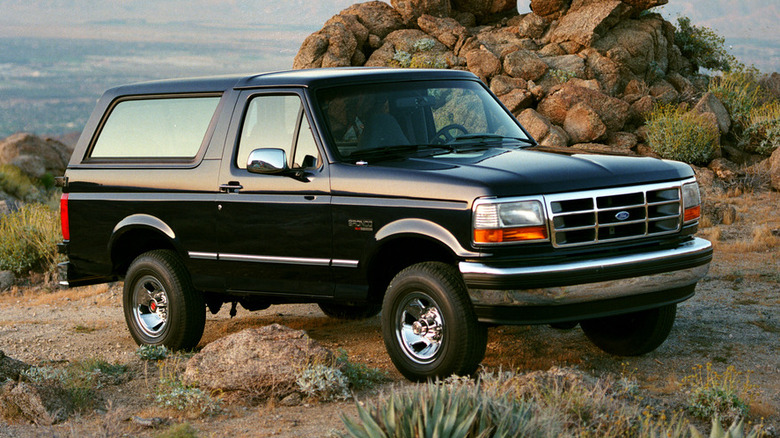 1994 Ford Bronco parked on a desert hilltop with a rocky background