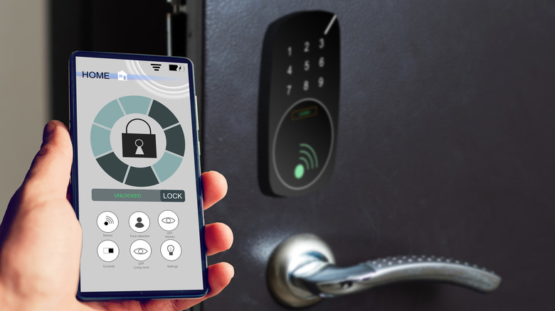 Hand holding a smartphone next to a smart door lock