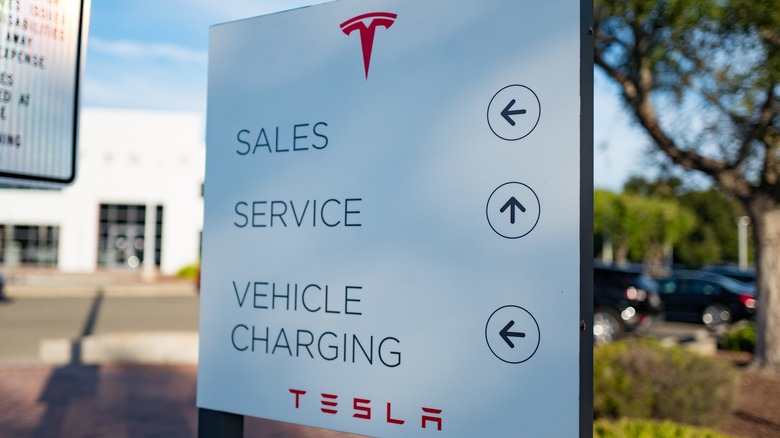 A sign at a Tesla dealership identifies the way to the sales and service departments, as well as vehicle charging.