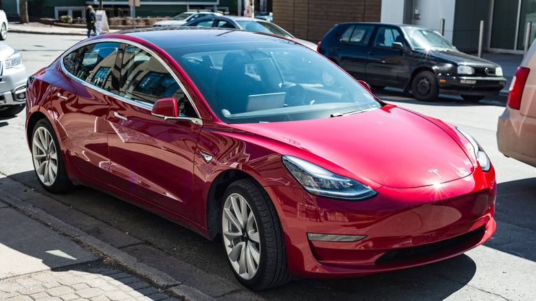 A red Tesla model 3 parked on the street