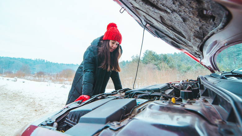 Woman looking under car hood in winter