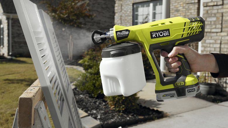 A person using a Ryobi paint sprayer on window trim