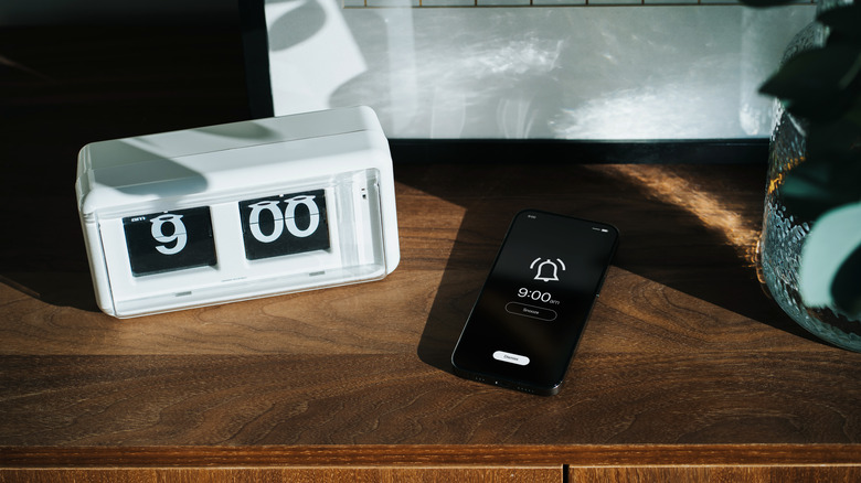 White alarm clock box and a black smartphone with an alarm