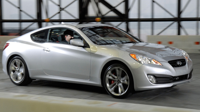 A Hyundai Genesis Coupe in silver driving, front 3/4 view