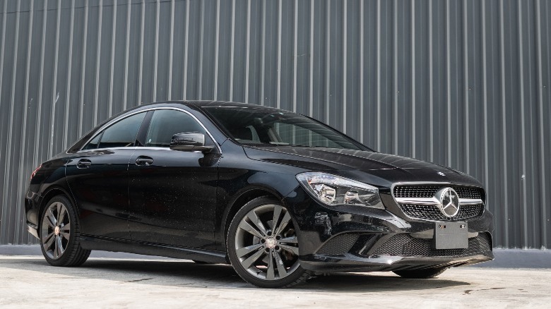 a black Mercedes-Benz sedan parked in front of a grey wall