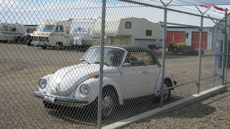 White convertible VW Super Beetle behind a fence