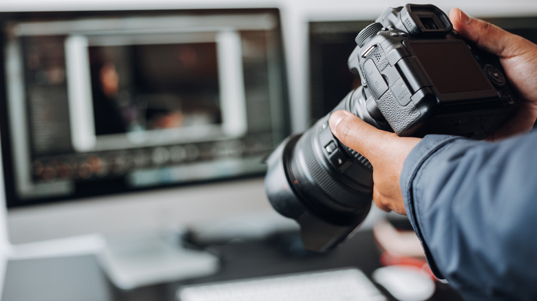 Hands holding a camera near a computer monitor