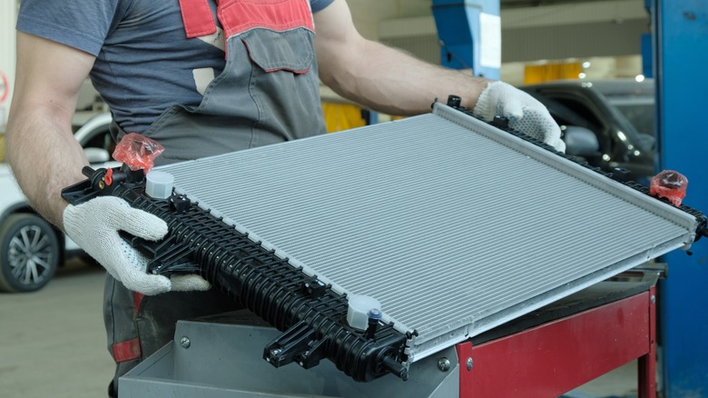 An auto mechanic holds a new engine cooling radiator in his hands