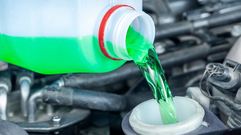 Close-up of pouring green anti-freeze liquid from the bottle to the coolant reservoir