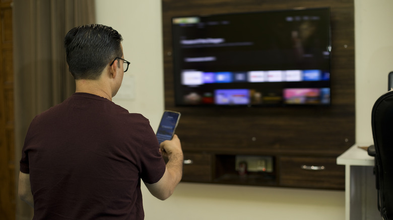 A man is watching TV with her smartphone