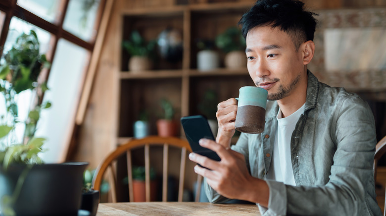 Man looking at his smartphone while drinking coffee