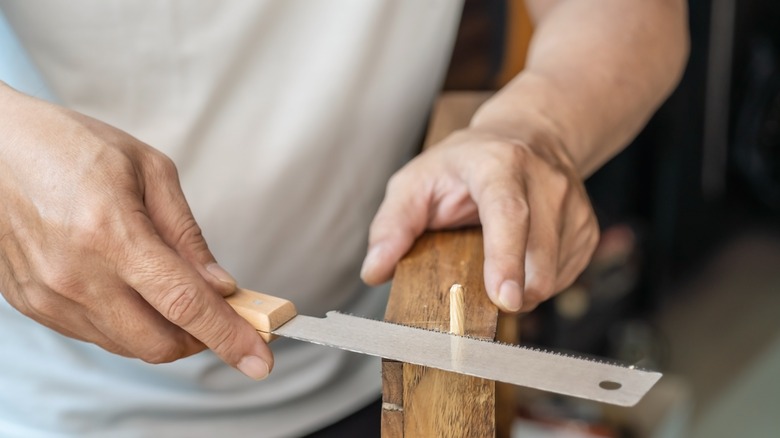 hands holding wood and Japanese pull saw sawing a dowel