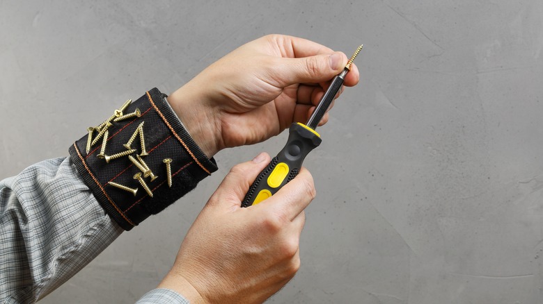 hands holding screwdriver and screw with magnetic wristband with screws