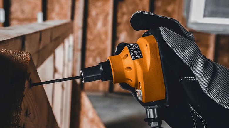 gloved hand holding an orange mini palm nailer