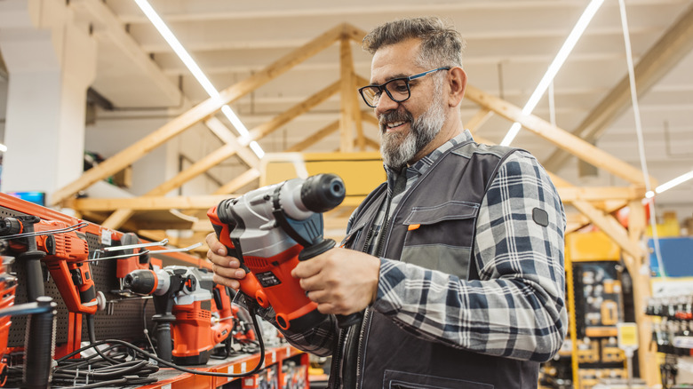 man with beard in hardware store holding and looking at a power tool