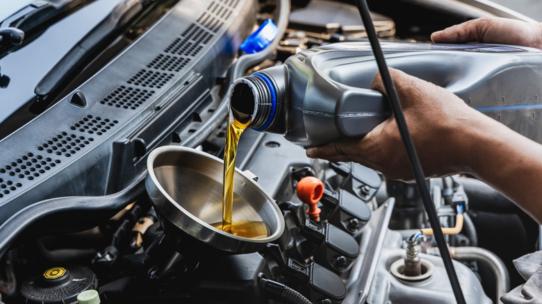 Car mechanic pouring engine oil into vehicle during doing car maintenance in garage