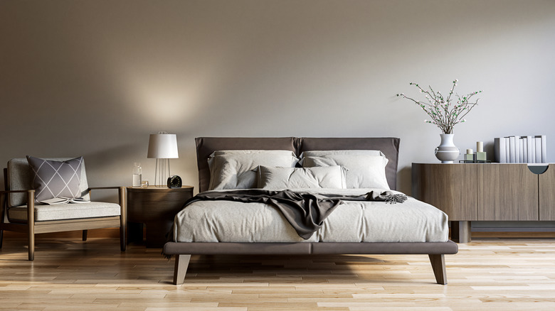 Serene bedroom in neutral colors featuring a bed, chair, dresser, and lamp