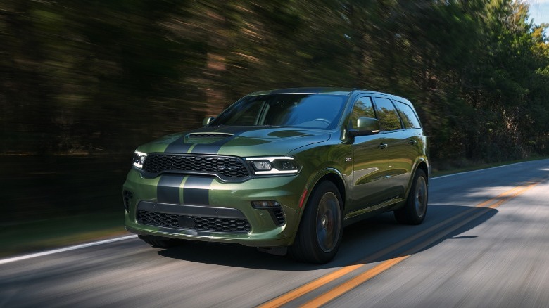 a green Dodge Durango SUV driving down a wooded road