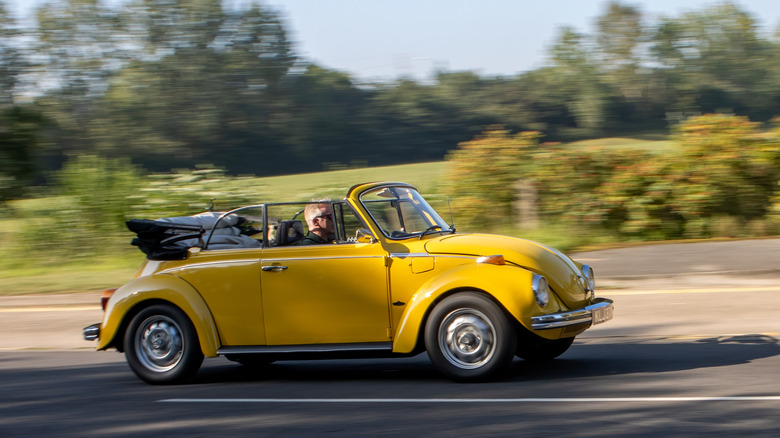 Person driving a yellow VW Beetle convertible