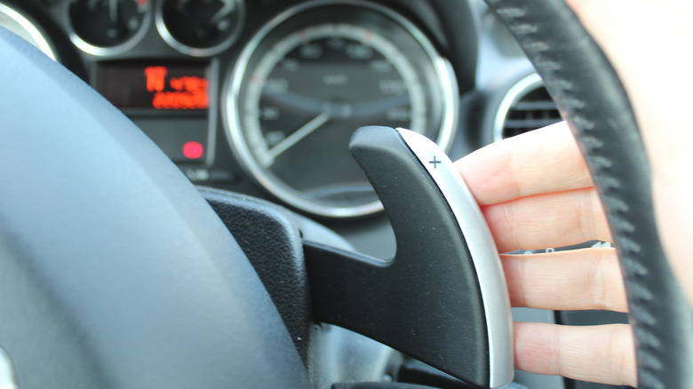 a person's hand using the paddle shifter, marked with a plus sign behind the steering wheel of a car