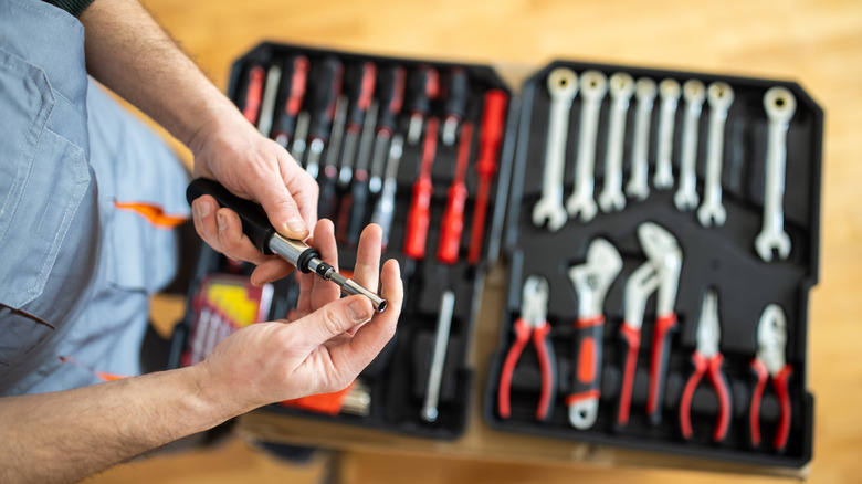 Unrecognizable repairman adjusting screwdriver after picking it from toolbox