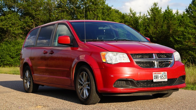 A red Dodge Caravan parked near trees