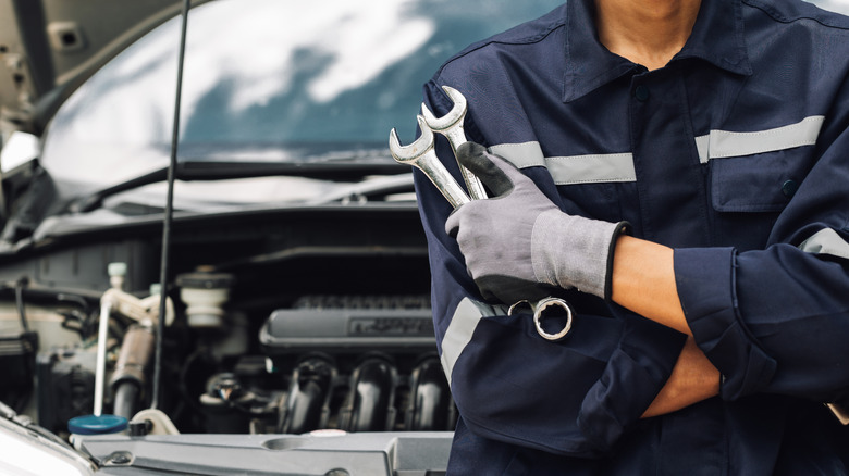 mechanic holding wrenches in front of car